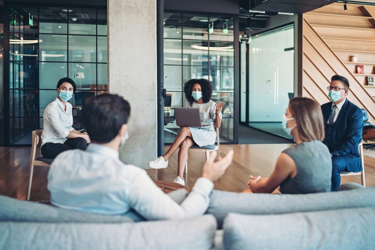 Group of entrepreneurs, wearing masks, sitting at a distance in the office and talking